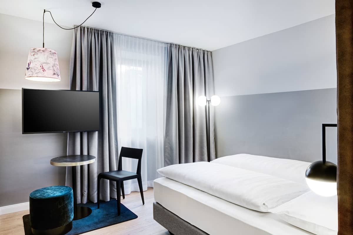 Een moderne hotelkamer met een groot bed, een flatscreen televisie aan de muur, een klein rond tafeltje, een stoel en een bureau.