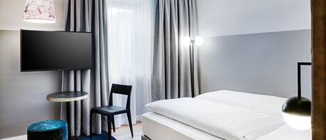 Een moderne hotelkamer met een groot bed, een flatscreen televisie aan de muur, een klein rond tafeltje, een stoel en een bureau.