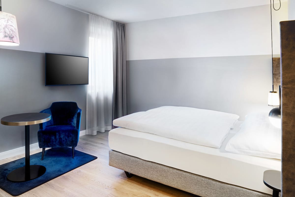 Een hotelkamer met een bed, een tv aan de muur, een blauwe stoel en een klein, rond tafeltje.