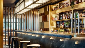 A bar area with a marble counter, stools, and shelves stocked with bottles.