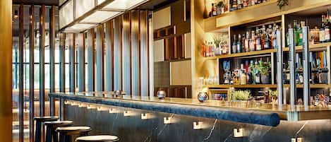 Un espace bar doté d’un comptoir en marbre, de tabourets et d’étagères remplies de bouteilles.