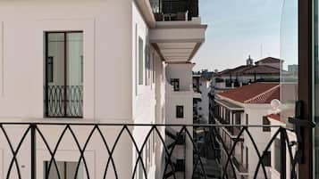Ein Balkon mit schmiedeeisernem Geländer, der auf eine Straße mit Häusern blickt.