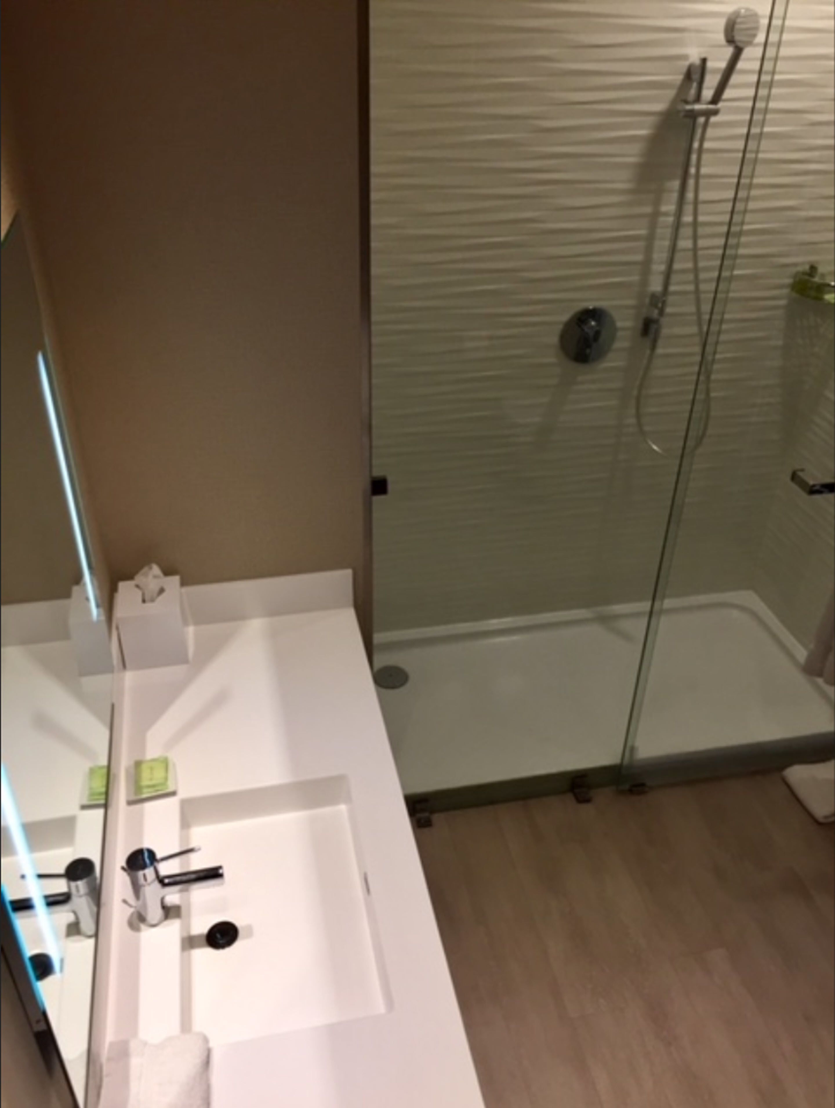 Ein Badezimmer mit Duschkabine aus Glas, einem weißen Waschbecken mit Spiegel und einem Handtuchhalter.