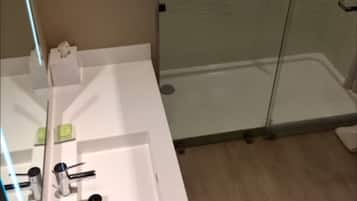 Ein Badezimmer mit Duschkabine aus Glas, einem weißen Waschbecken mit Spiegel und einem Handtuchhalter.