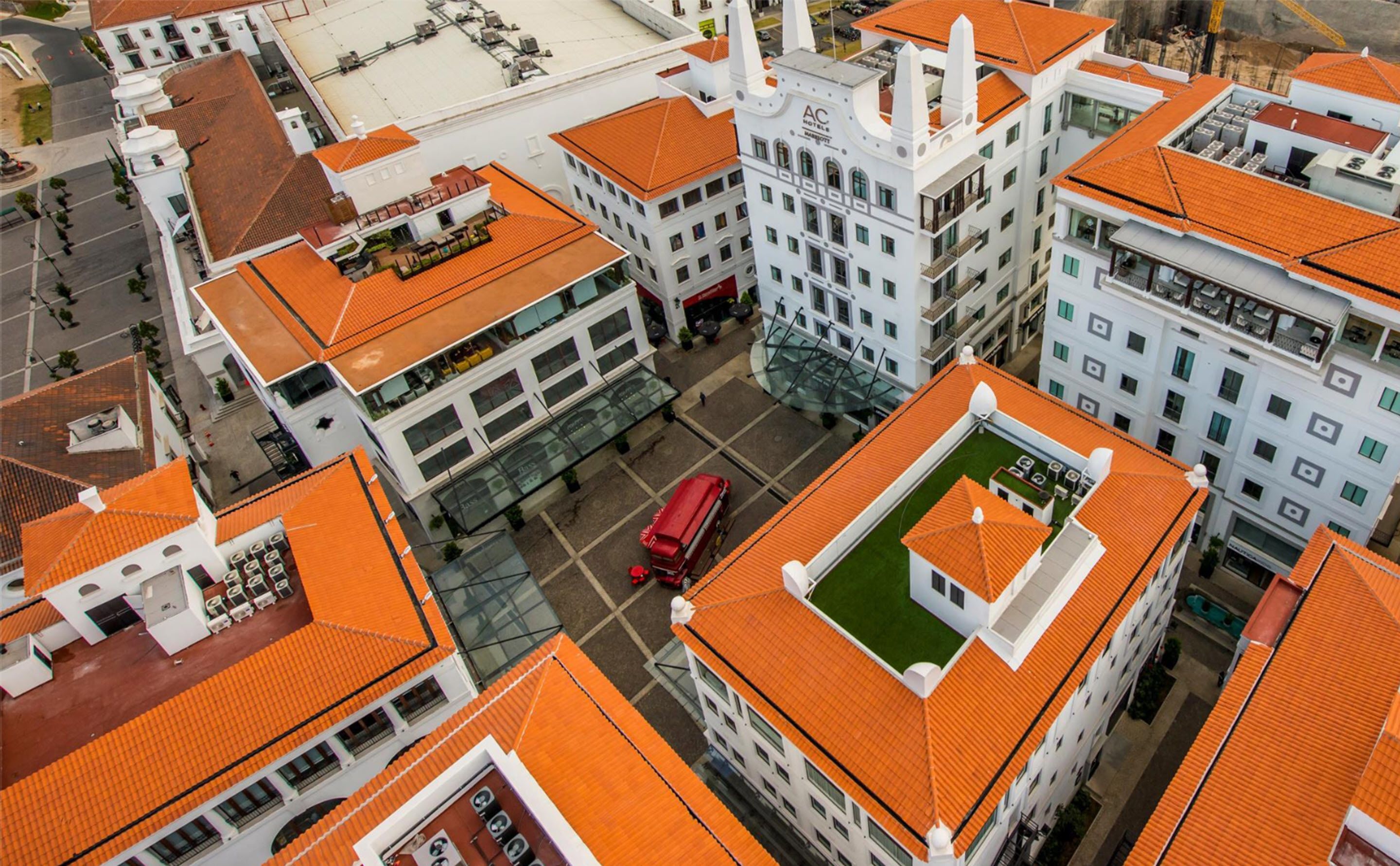 Un hôtel de grande hauteur, avec des toits recouverts de tuiles orange, de nombreux étages et une cour intérieure où se trouve un autobus rouge.