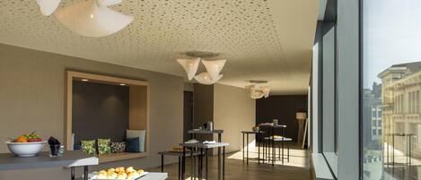 A modern interior with a dining area, a large window with a city view, and a ceiling with a perforated pattern.