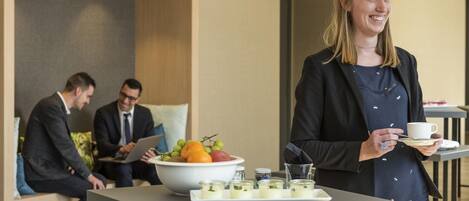 A woman holding a cup and tray with food and drinks, with two men in the background.