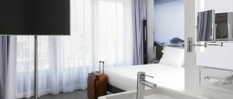 A hotel room with a bed, a TV, a bathroom with a sink, and a suitcase.