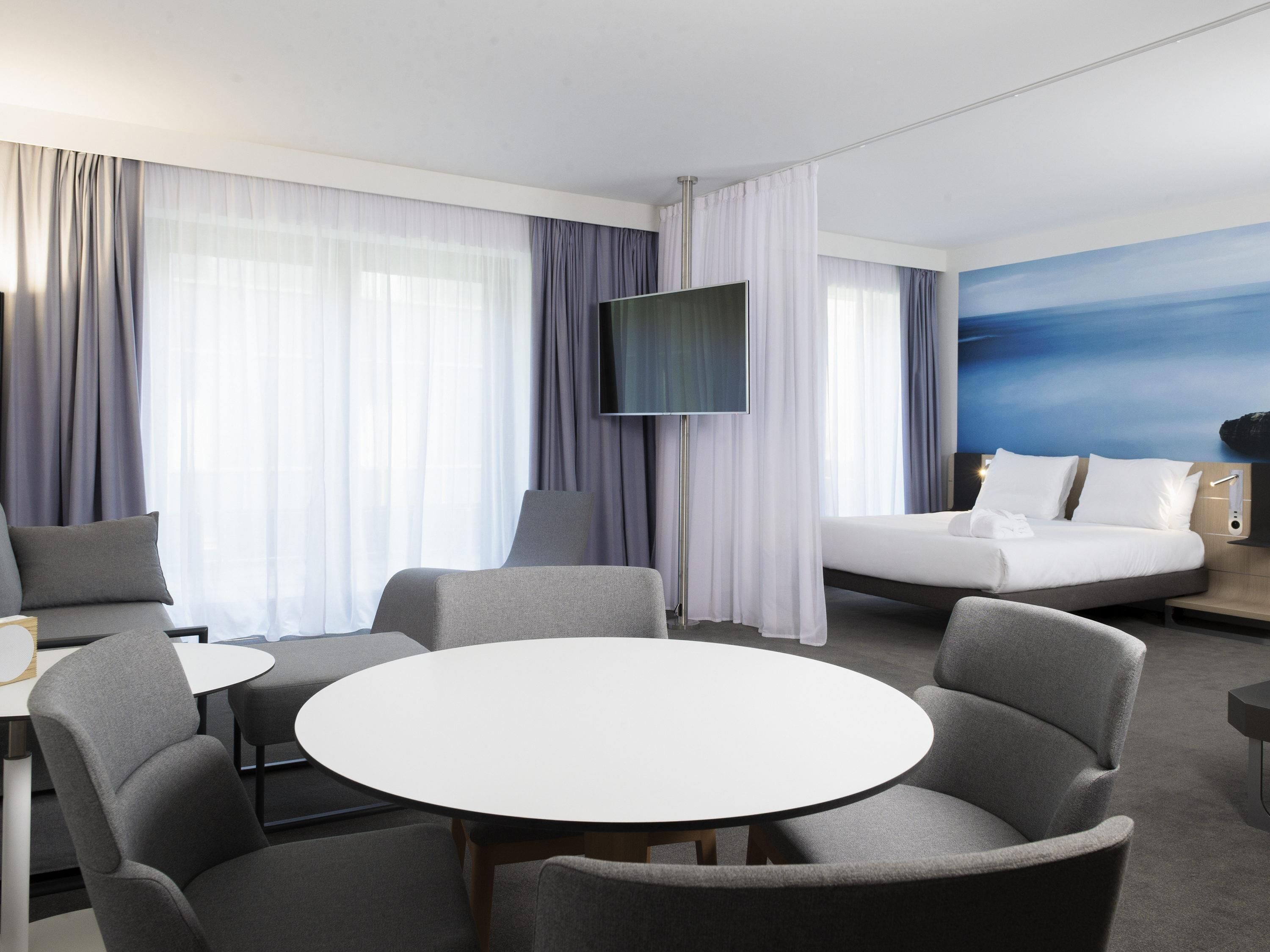 A hotel room with a bed, a TV, a round table, and two armchairs.