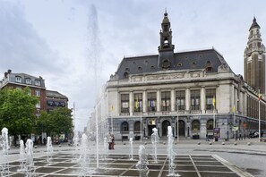 Um edifício histórico com uma fonte em frente, janelas amplas e bandeiras.