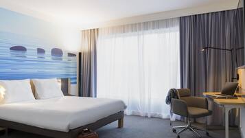 Habitación de hotel con cama, escritorio, silla y vista al mar.
