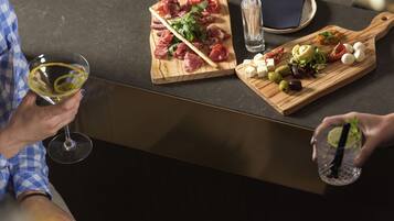 A person holding a wine glass, a wooden board with various cheeses and olives, and another person with a drink.