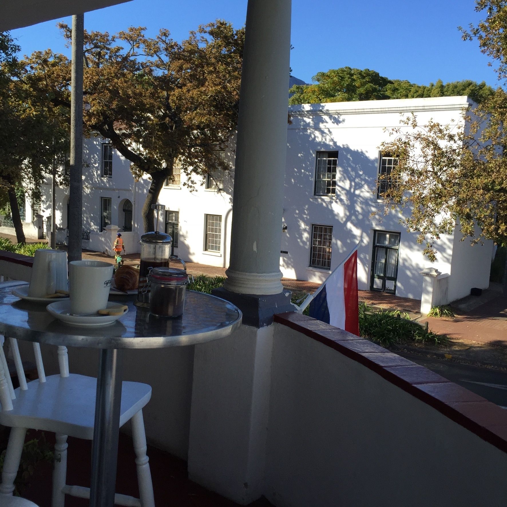 An outdoor seating area with white chairs and tables, a flag, and a building with white walls and windows in the background.