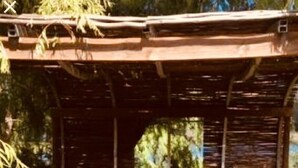 Una estructura de madera rústica con un banco y una mesa, rodeada de hierba alta y árboles.