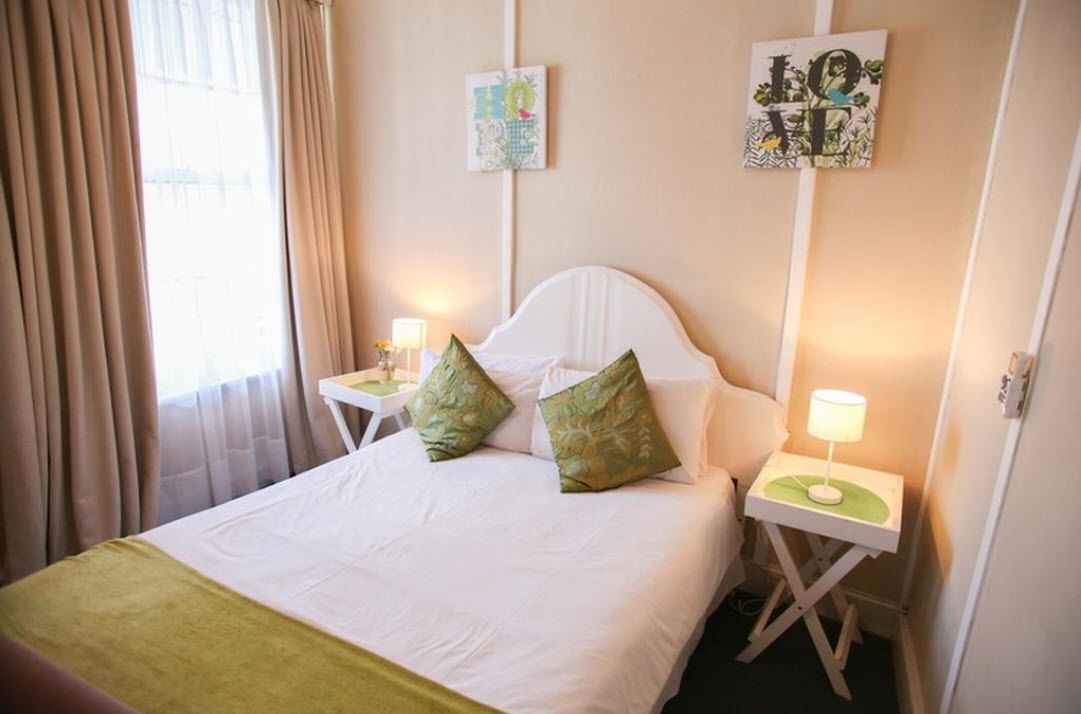Una cama bien hecha con dos almohadas, una mesita de noche con una lámpara y dos cuadros decorativos en la pared.