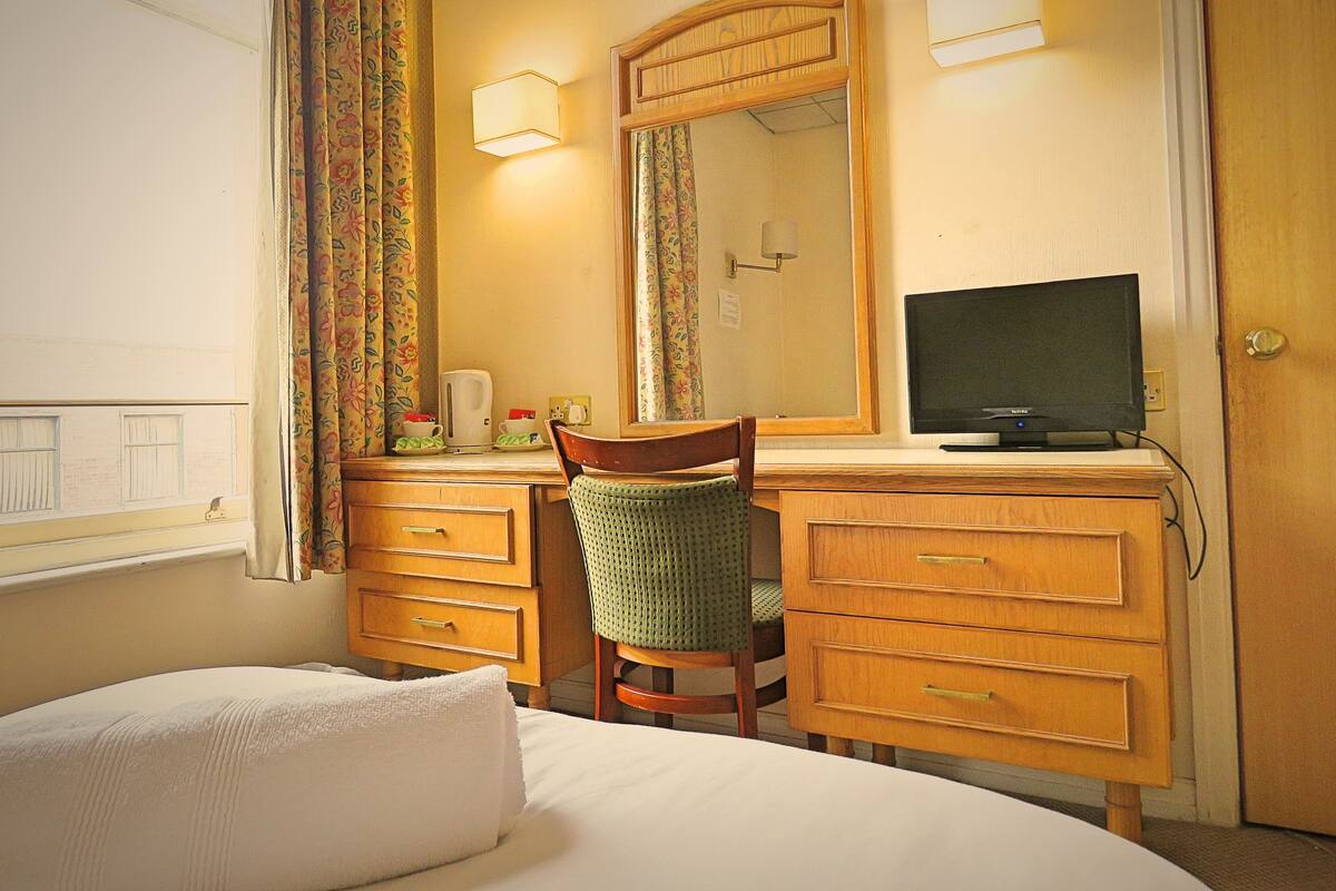 A hotel room with a bed, a desk with a chair, a television, and a mirror.