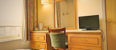 Una habitación de hotel con cama, escritorio, silla, televisor y espejo.