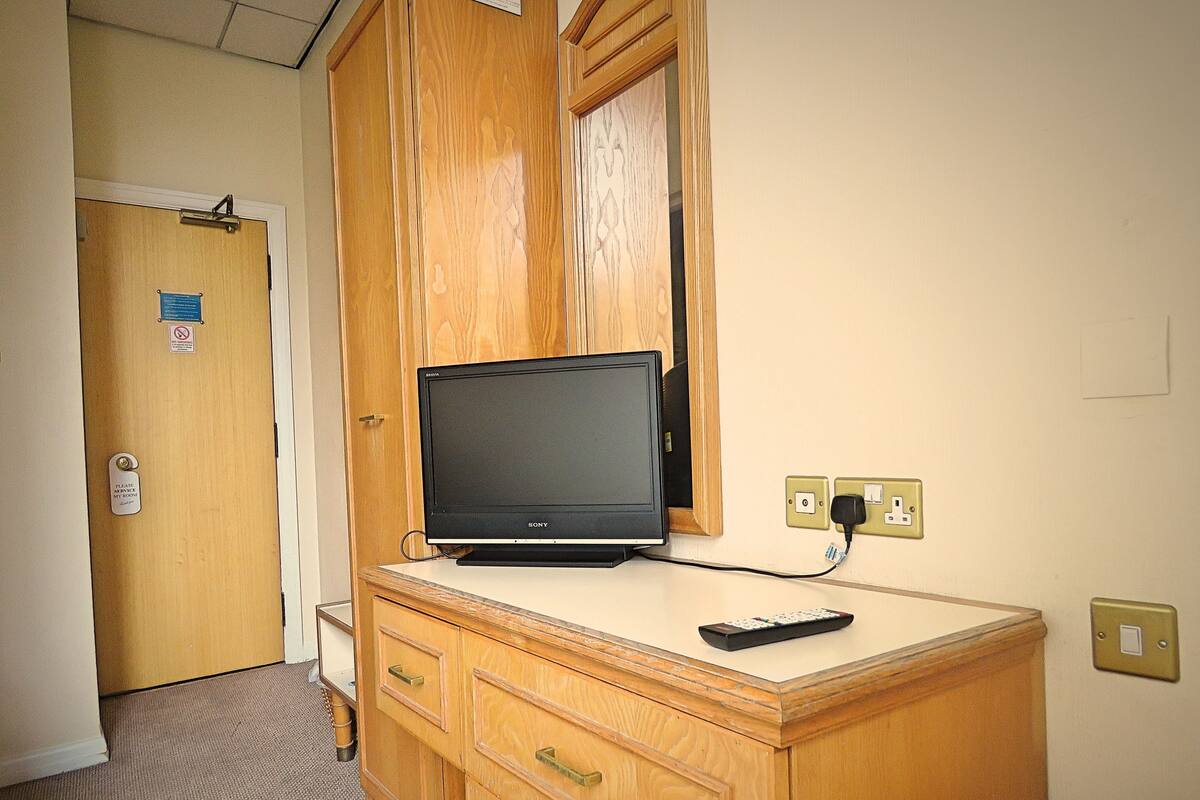 A wooden desk with a television, a remote control, and a power outlet.