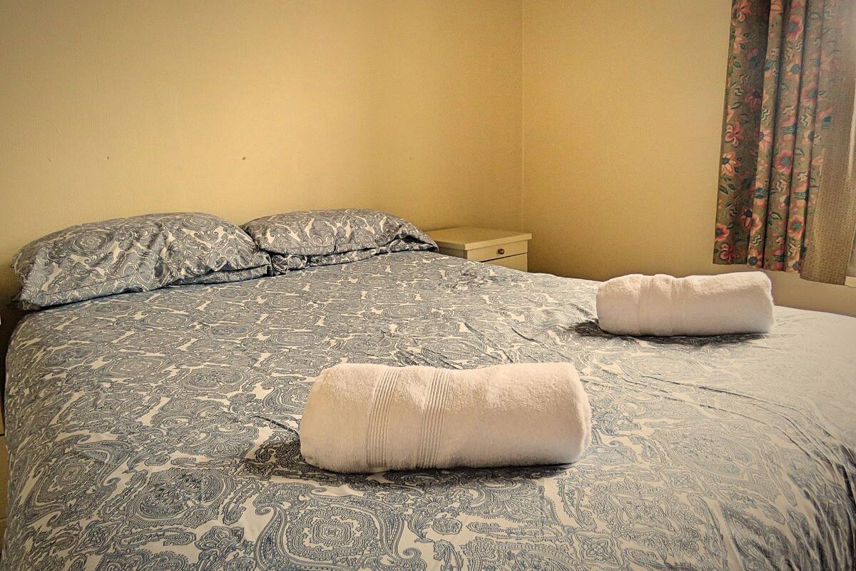 A neatly made bed with patterned bedding and two rolled towels.