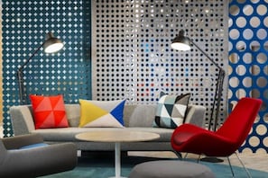 A modern lounge area with a sofa, a red chair, and a round table. - Holiday Inn Express Astana - Turan (Astana)