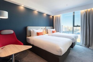 A hotel room with two beds, a desk, a chair, a lamp, and a large window with curtains. - Holiday Inn Express Astana - Turan (Astana)