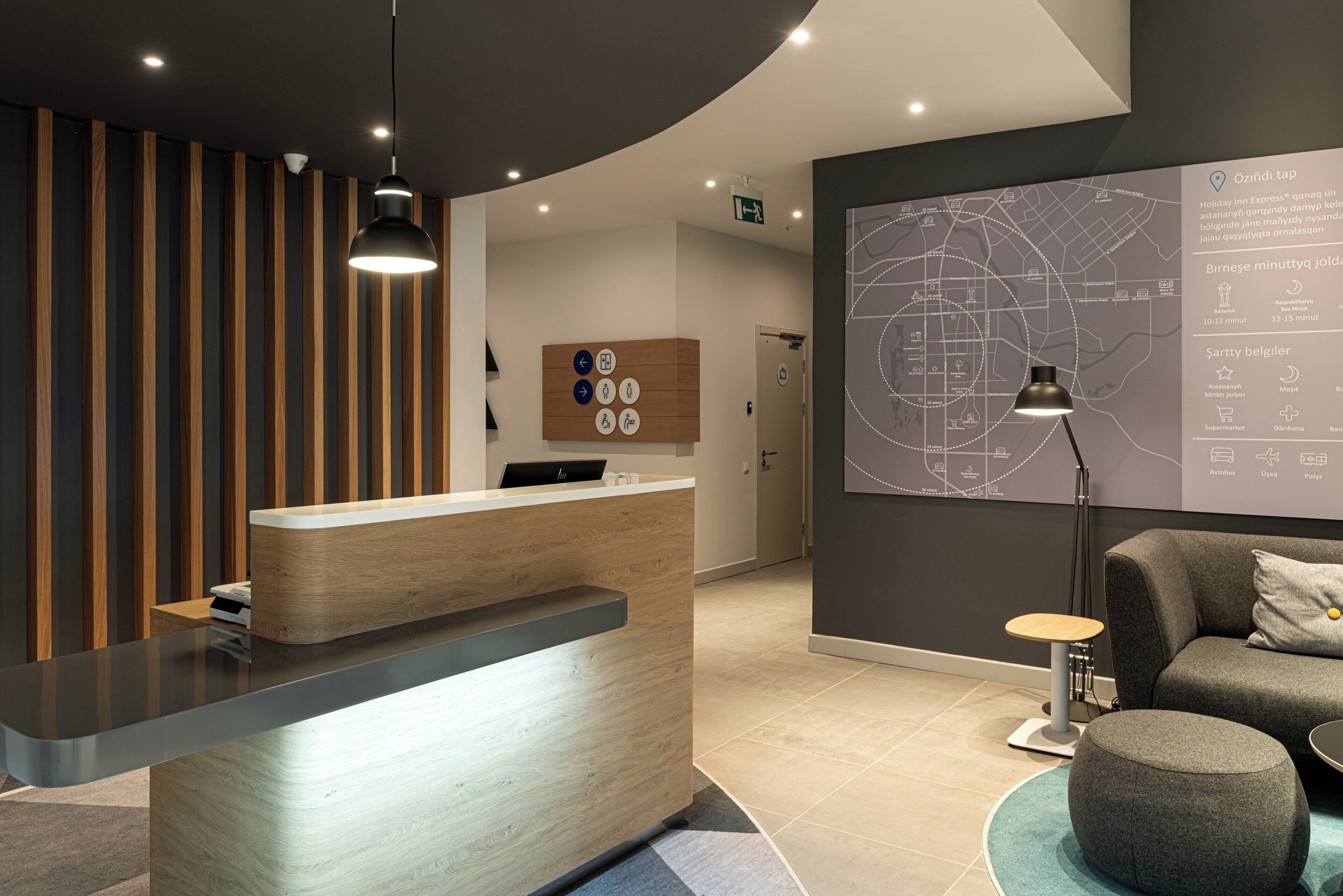 A modern reception desk with a wooden finish, a map on the wall, and a seating area with a round table and ottoman.