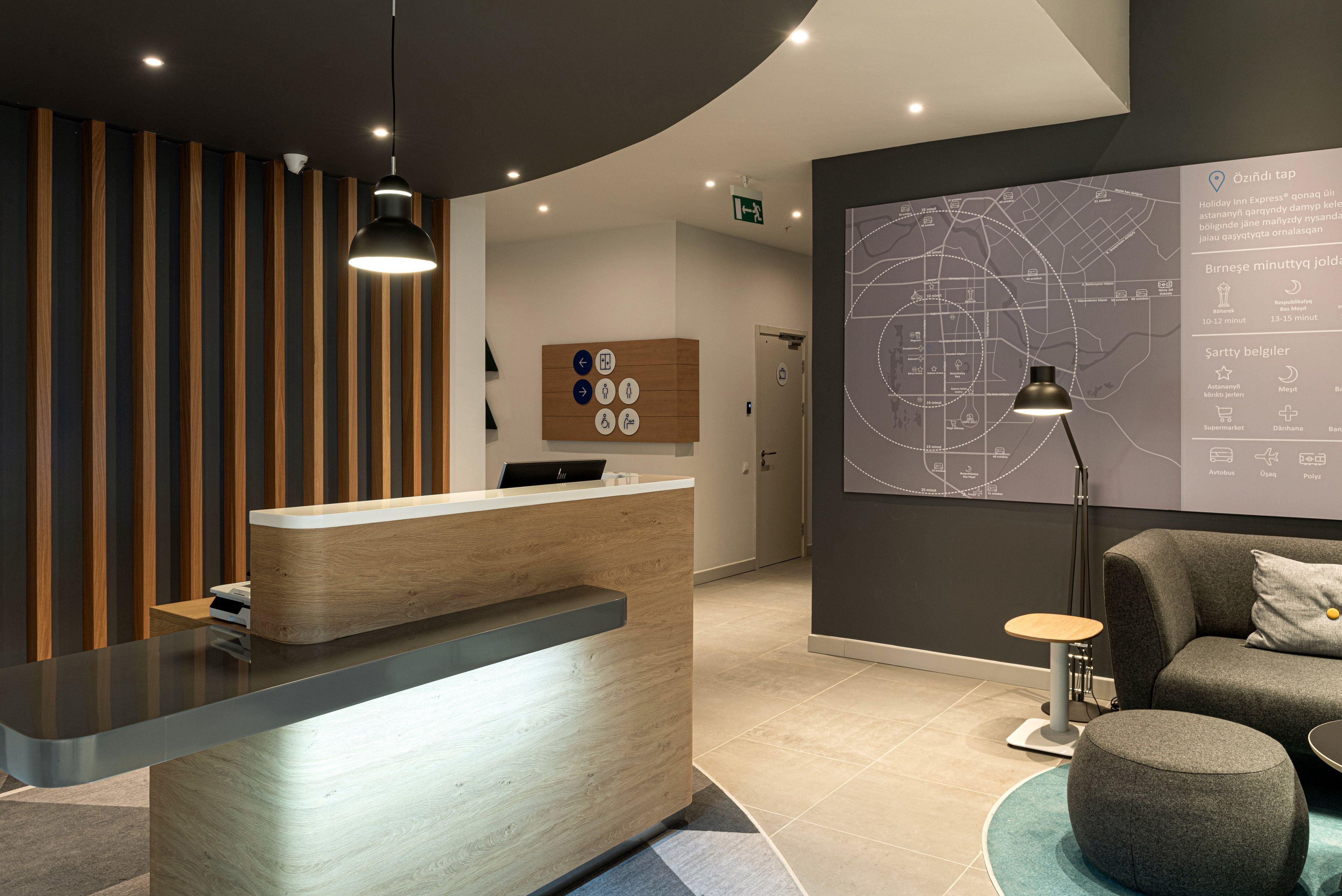 A modern reception desk with a wooden finish, a map on the wall, and a seating area with a lamp.