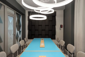 A conference room with a blue table, grey chairs, and a modern ceiling light fixture.