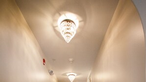 Un pasillo con piso de madera, paredes blancas y un candelabro. Hay dos cuadros enmarcados en la pared y una puerta blanca al final.