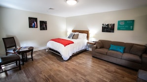 Habitación de hotel con cama, sofá, sillón y una pequeña mesa. Hay cuadros en la pared y un cartel que indica el camino al Puente Golden Gate.