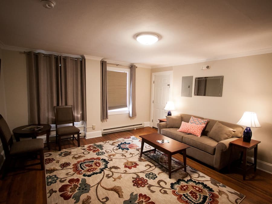 A living room with a sofa, two chairs, a coffee table, and a patterned rug.