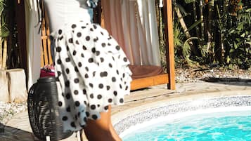 Eine Person in einem Punktekleid in der Nähe eines Pools mit Holzterrasse und tropischen Pflanzen.