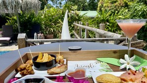 A tropical outdoor dining area with a variety of snacks and a martini on a wooden table. - Eden Paradise Spa Ecolodge (Sainte-Luce)