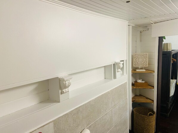 A bathroom with white walls, a tiled floor, and a wooden shelf with a decorative item.