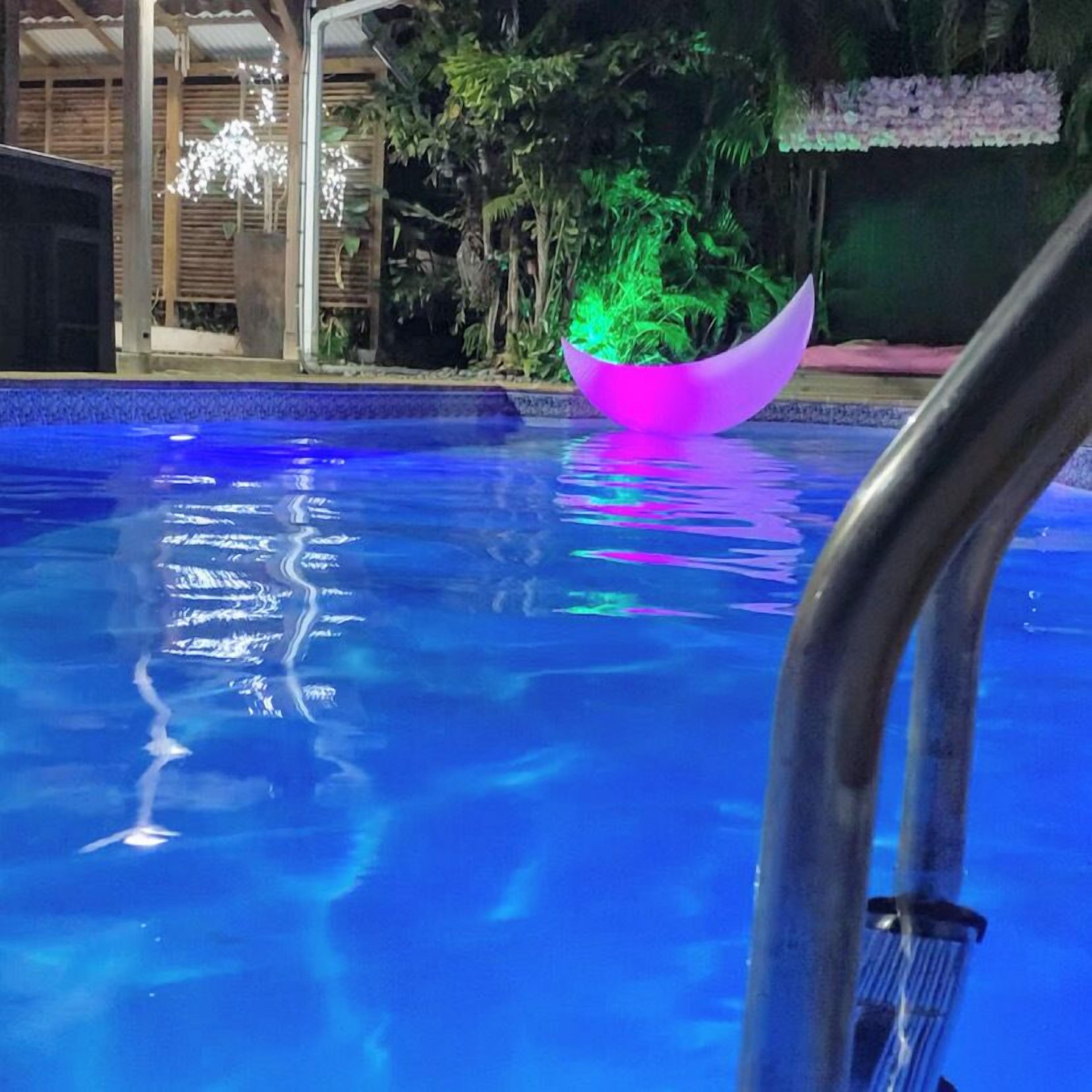 Una piscina con una fuente iluminada en tonos rosa y verde.
