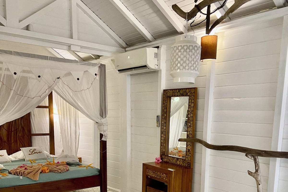 A bedroom with a canopy bed, a wooden dresser, a mirror, and a bathtub.