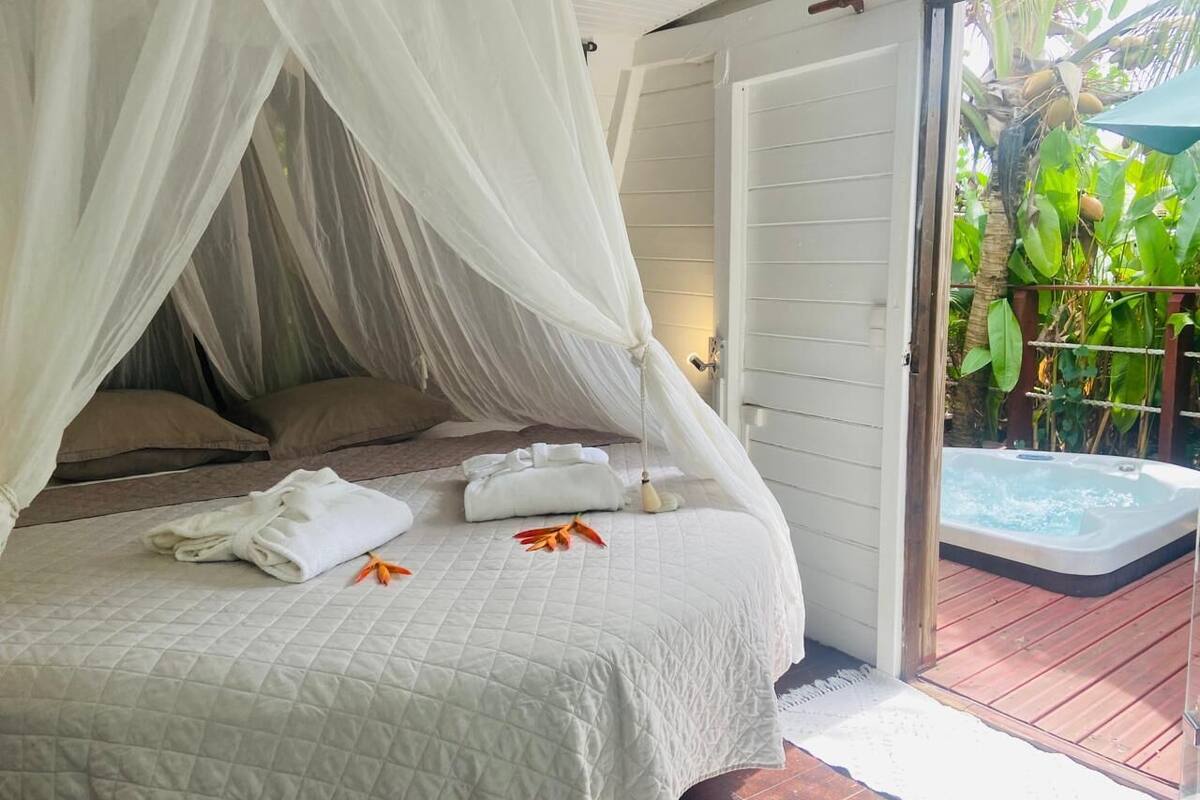 A bedroom with a bed, white bedding, a canopy, and a view of a hot tub outside.