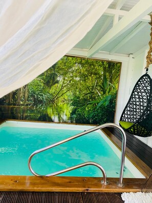 A pool area with a metal ladder, a hanging chair, and a mural of a forest scene.