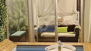 A room with a glass partition, a bed with pillows, a bench, and a small table with a basket. - Eden Paradise Spa Ecolodge (Sainte-Luce)