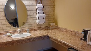 A bathroom with a granite countertop, a sink, a mirror, a towel rack, a tissue box, and a stainless steel refrigerator. - Northwoods Motel (Hayward)