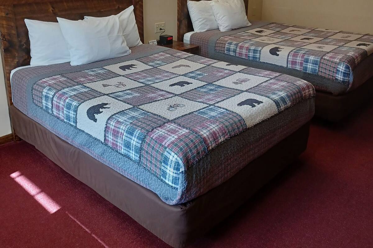 A hotel room with two beds, each with a quilted blanket featuring animal prints. There are wall-mounted lights and two paintings above the beds.