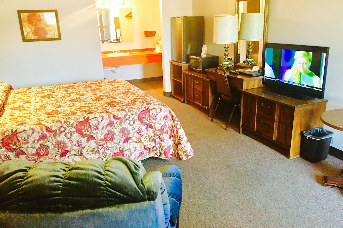 Ett hotellrum med en säng, ett skrivbord med en dator, en tv och en papperskorg.