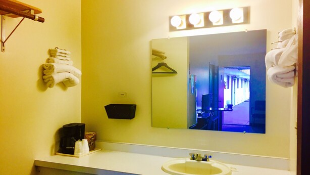 Un baño con lavabo, espejo, perchero para toallas y una bolsa colgada.