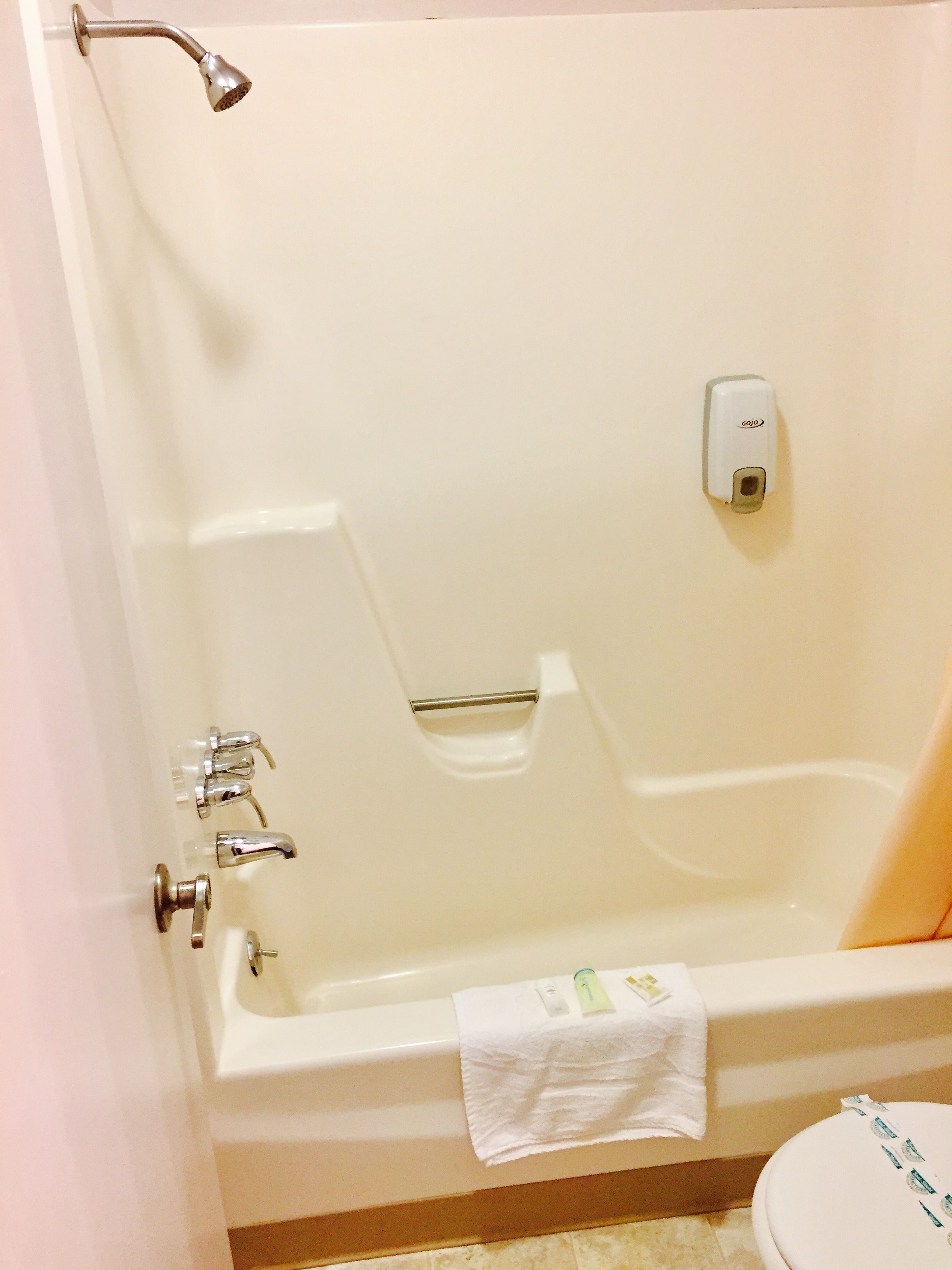 A bathtub with a handheld showerhead, a soap dispenser, and a towel on the side.