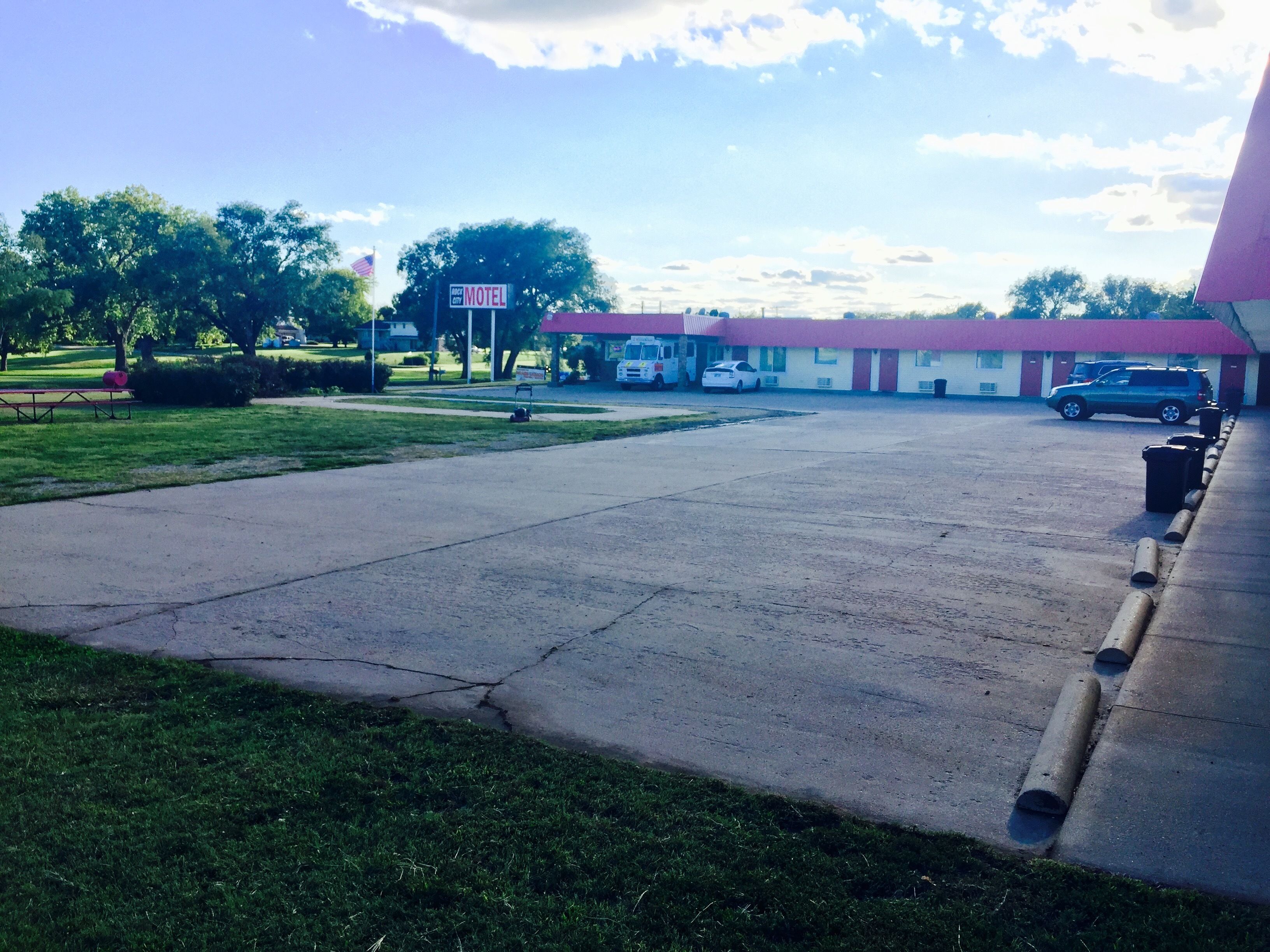 Um motel com teto vermelho, estacionamento e área gramada.