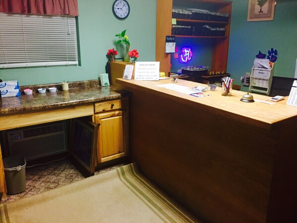 A hotel reception desk with a clock, a neon sign, and a sign indicating pet fees. - Rock City Motel (Minneapolis)