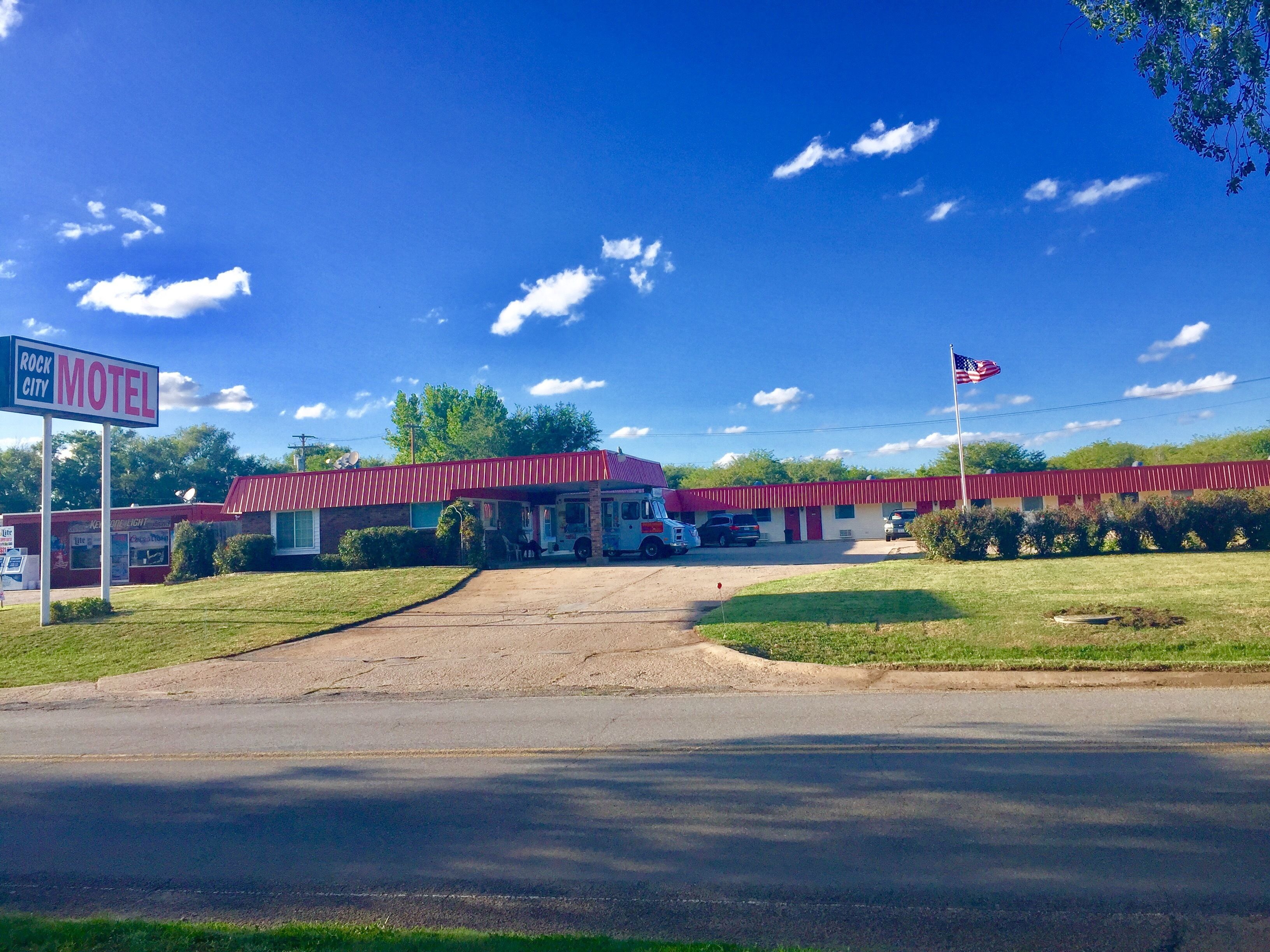 Un motel con fachada roja y blanca, un estacionamiento y una bandera estadounidense.