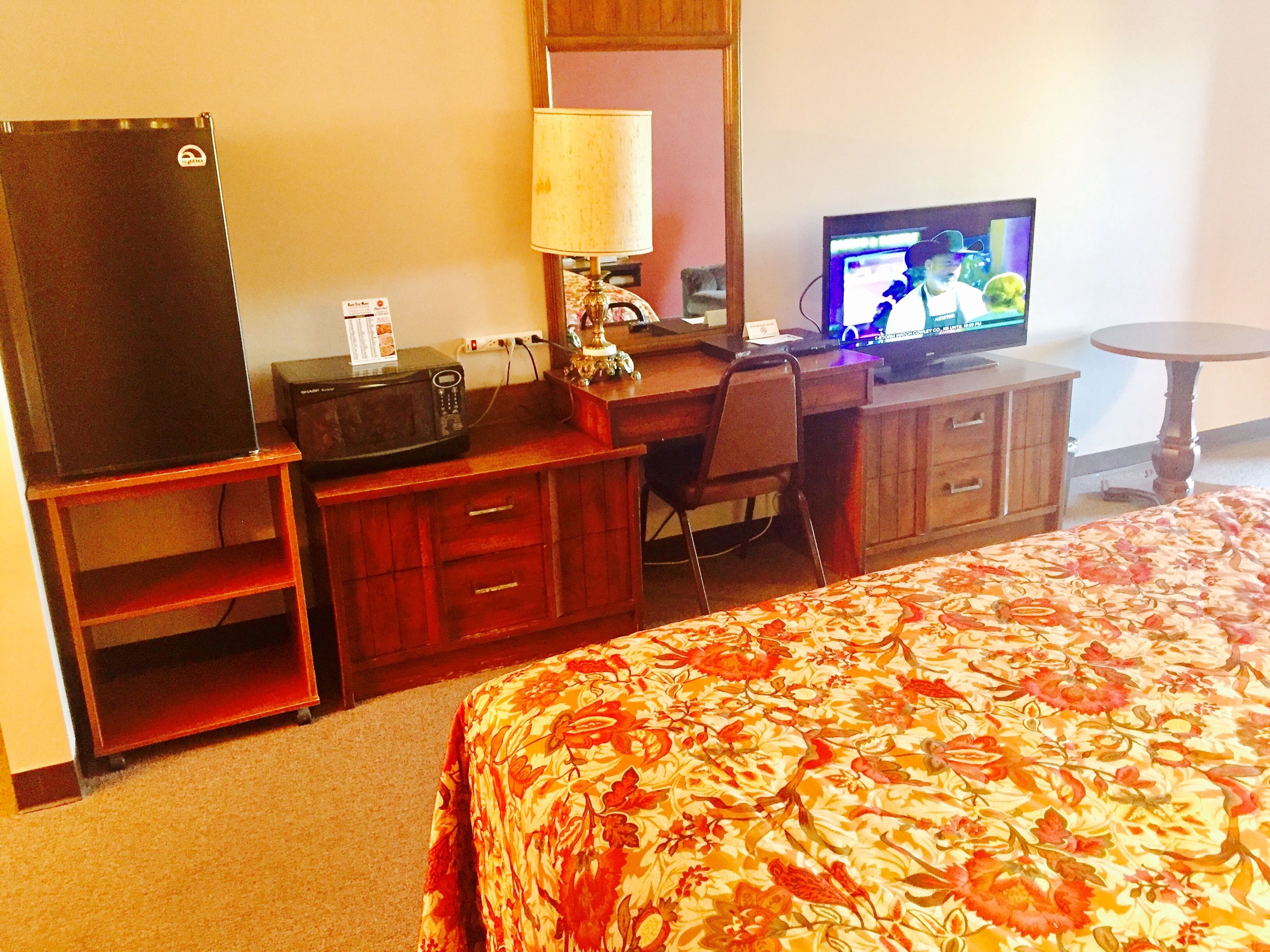 A hotel room with a bed, a desk with a computer, a television, and a refrigerator.