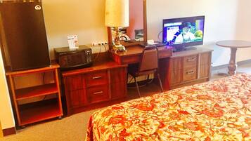 A hotel room with a bed, a desk with a computer, a television, and a refrigerator.