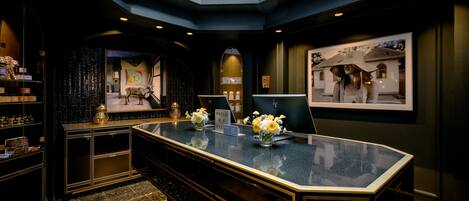 A modern hotel lobby with a marble reception desk, a large framed picture on the wall, and a decorative archway.